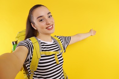 Photo of Smiling young woman with backpack taking selfie on orange background, space for text. Active tourism