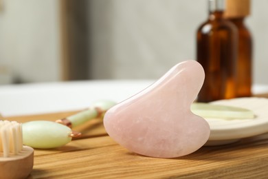 Jade and rose quartz gua sha tools, natural face roller with cosmetic product on wooden bath caddy, closeup