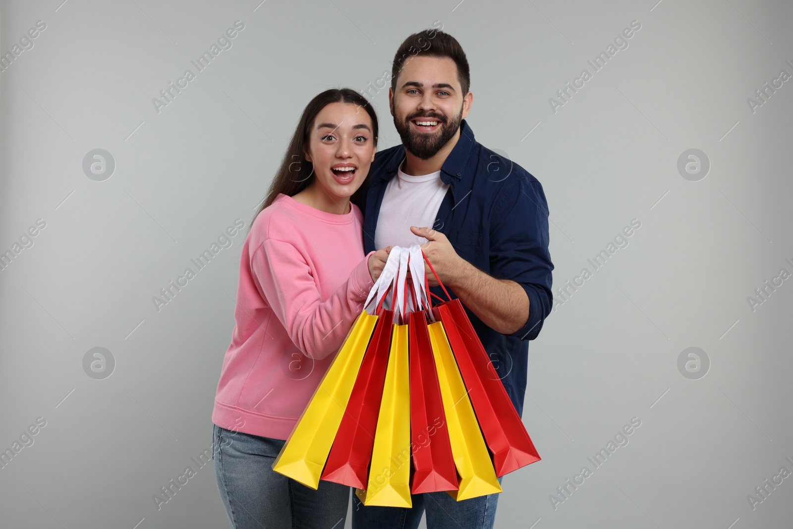 Photo of Excited couple with shopping bags on grey background