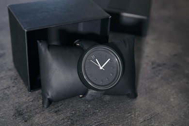 Photo of Small decorative pillow with stylish wrist watch and box on gray table. Fashion accessory