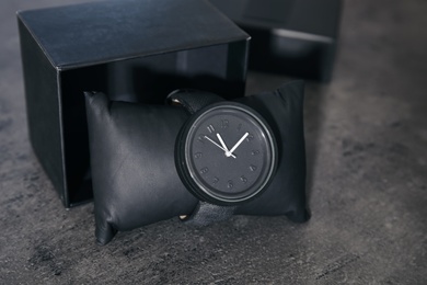 Small decorative pillow with stylish wrist watch and box on gray table. Fashion accessory