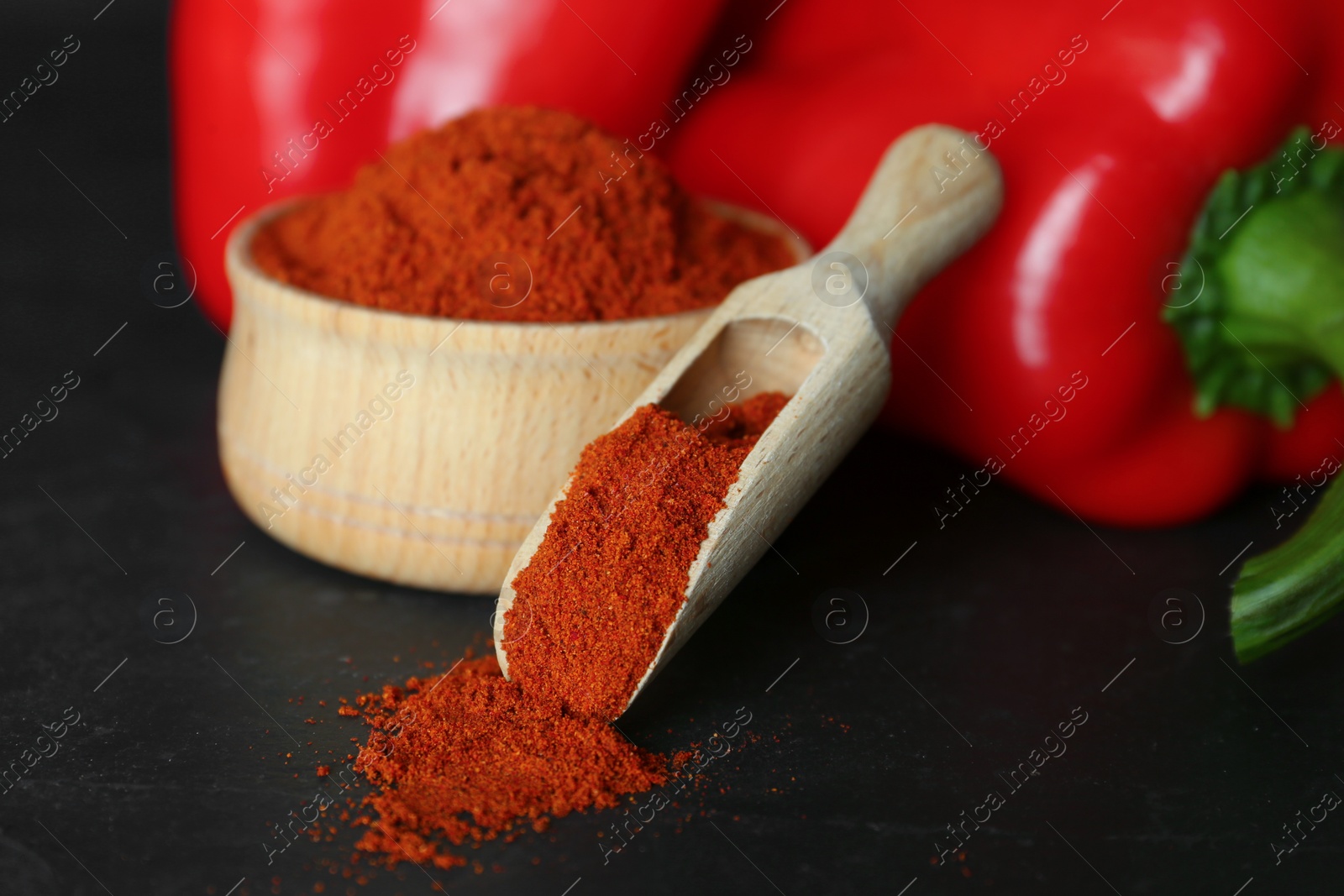 Photo of Paprika powder and fresh bell peppers on black table, closeup