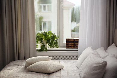 Photo of Comfortable bed with pillows and blanket near window