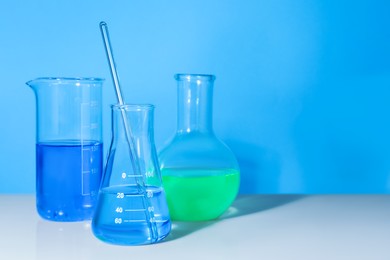 Glass flasks with colorful liquids on white table against light blue background. Space for text