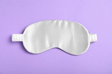 Photo of White sleeping mask on violet background, top view. Bedtime accessory
