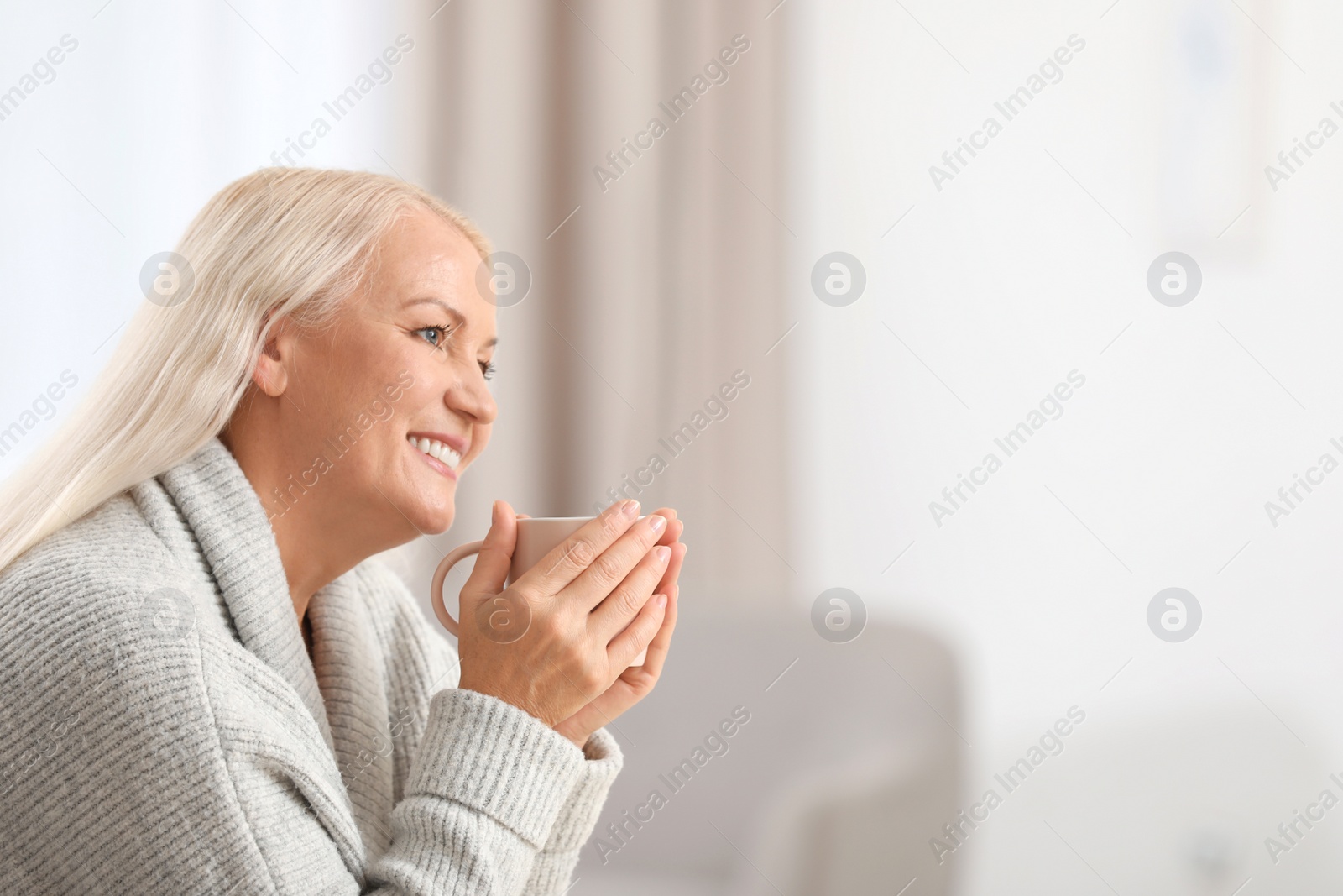 Photo of Portrait of beautiful older woman with cup of tea against blurred background. Space for text