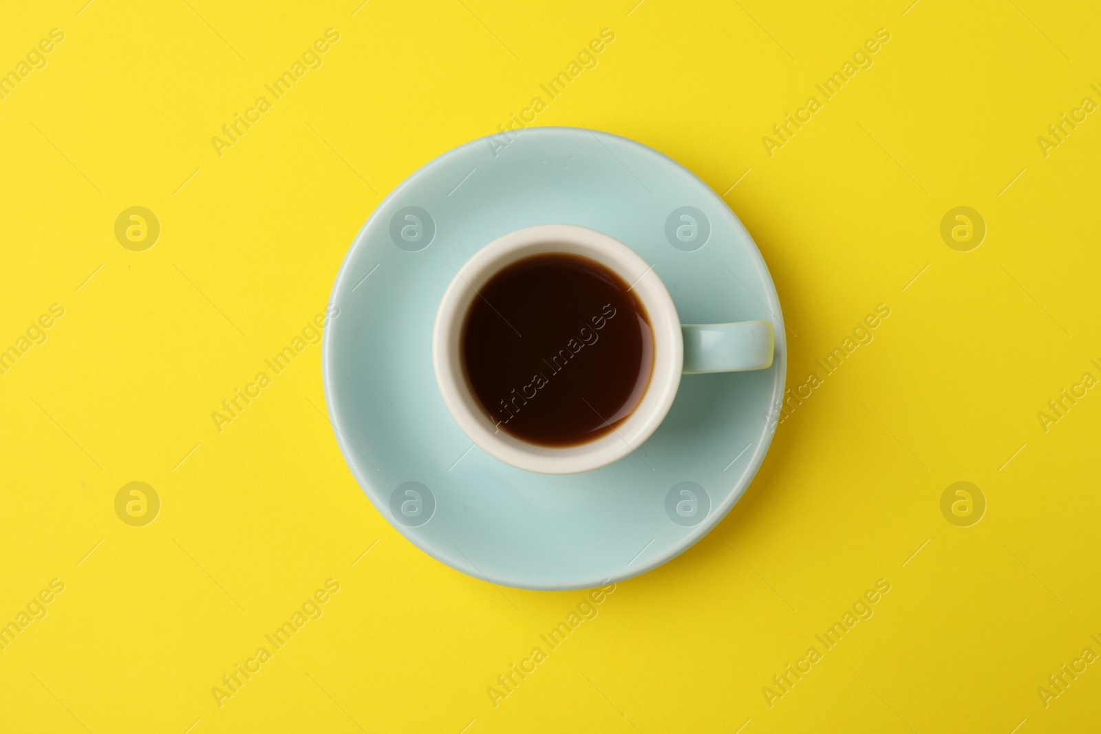 Photo of Tasty coffee in cup on yellow background, top view