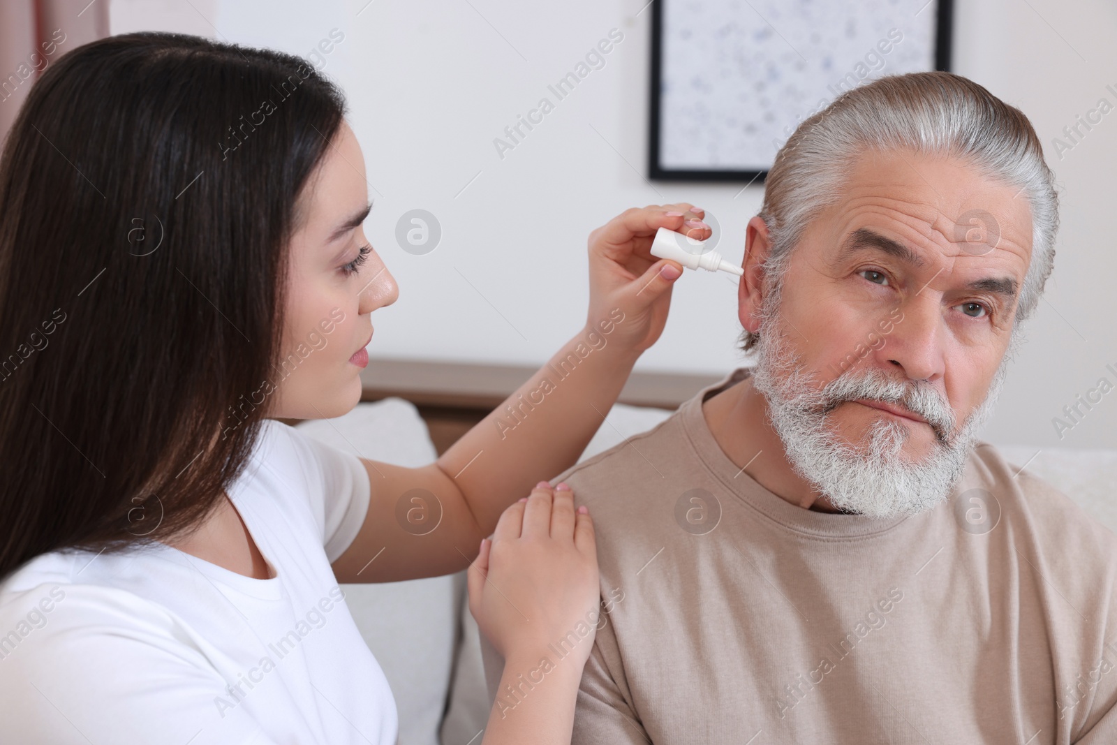 Photo of Young woman dripping medication into man's ear at home