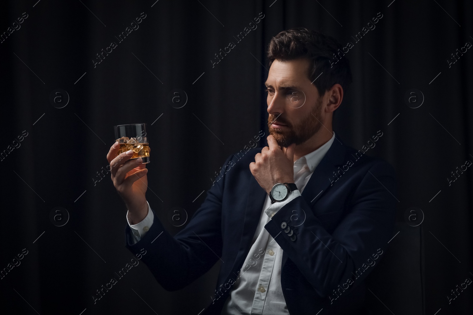 Photo of Handsome man in suit holding glass of whiskey on black background