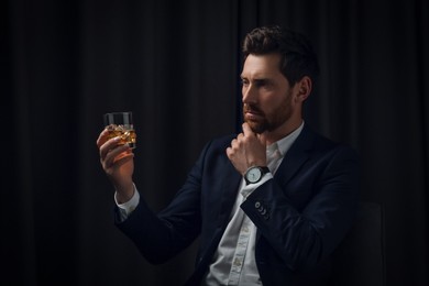 Handsome man in suit holding glass of whiskey on black background