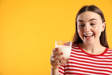 Photo of Emotional woman with milk mustache holding glass of tasty dairy drink on orange background, space for text