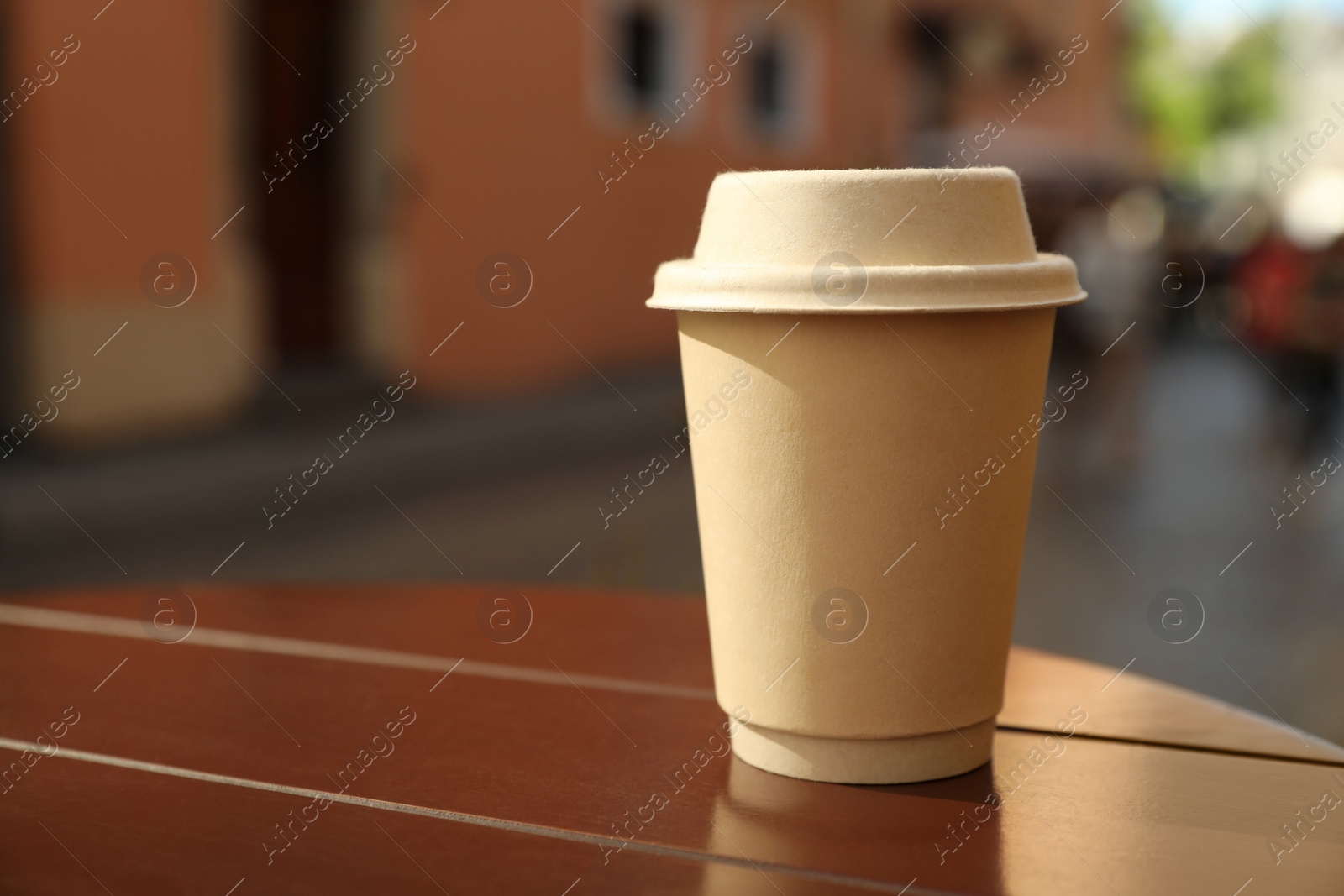 Photo of Cardboard takeaway coffee cup with lid on wooden table in city, space for text