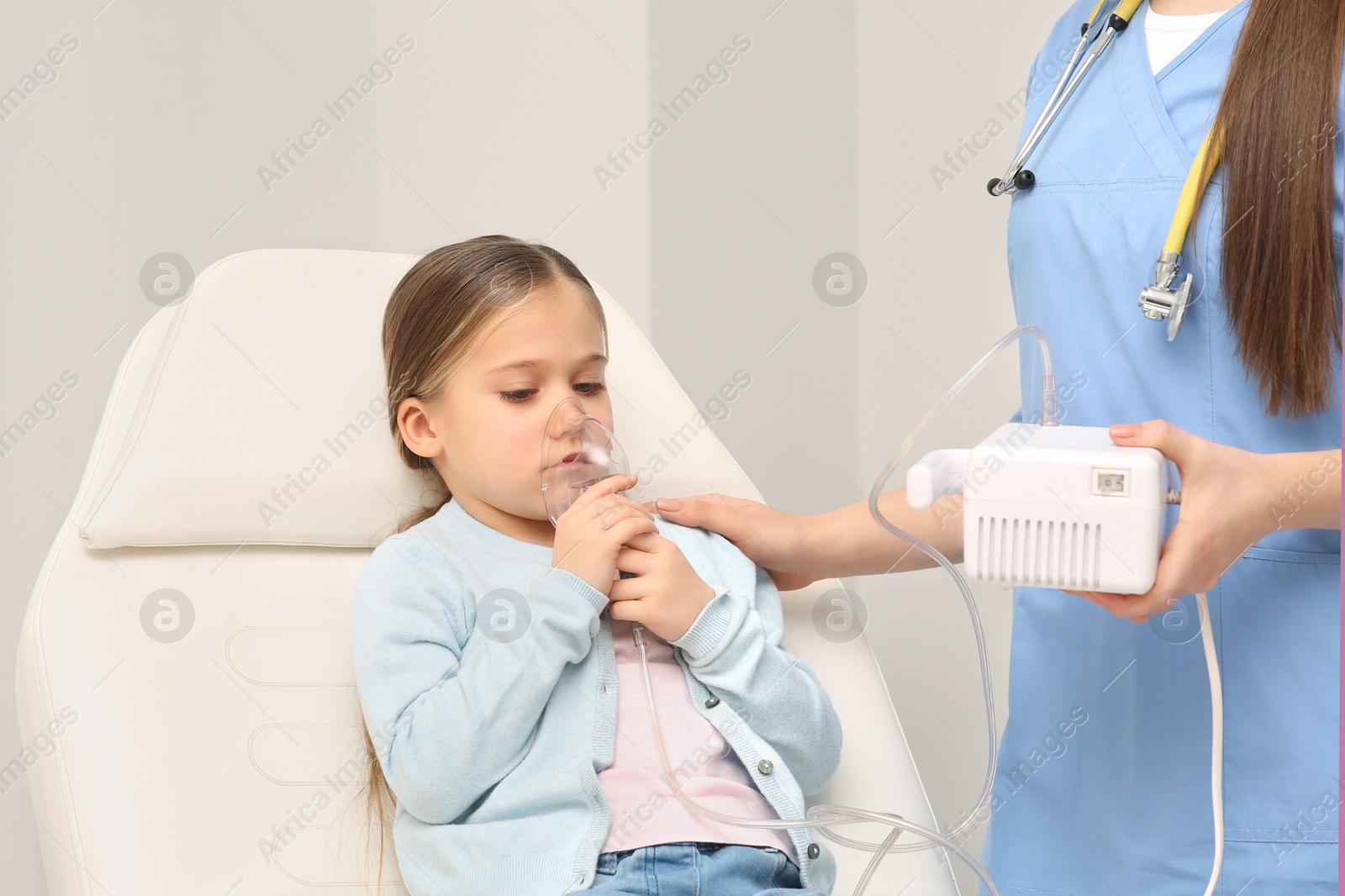 Photo of Medical assistant helping sick little girl with nebulizer inhalation in hospital