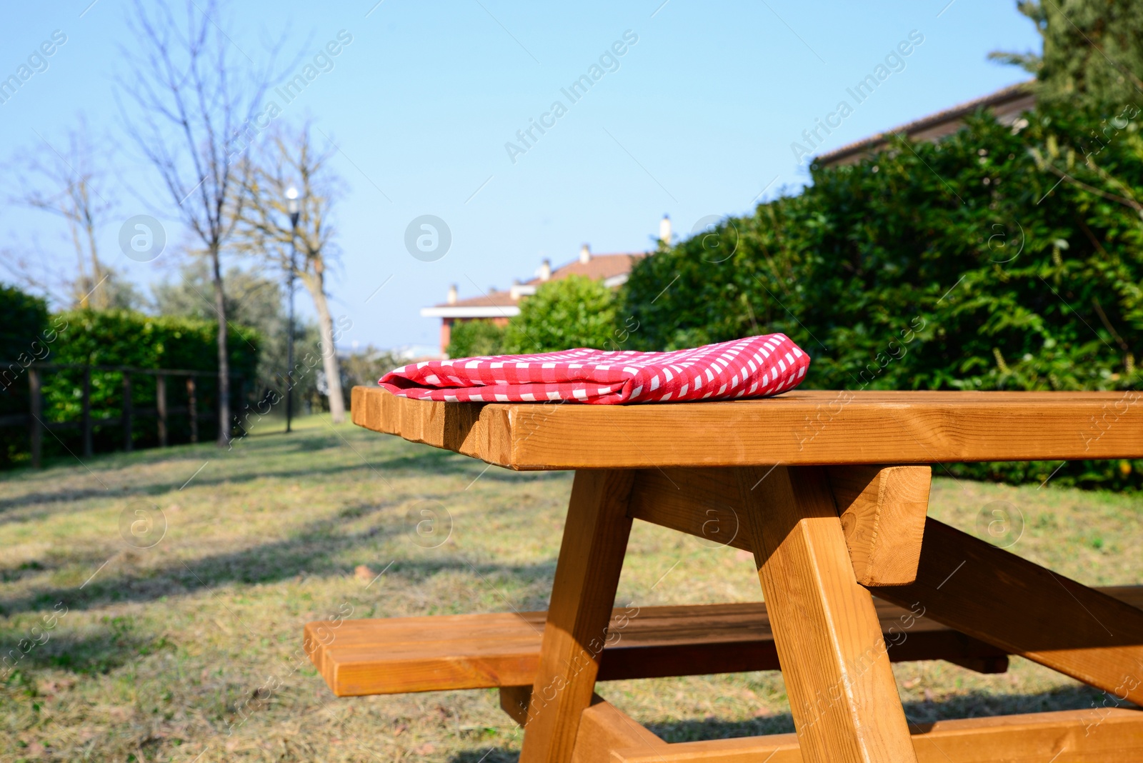 Photo of Folded red and white checkered tablecloth on wooden picnic table in backyard