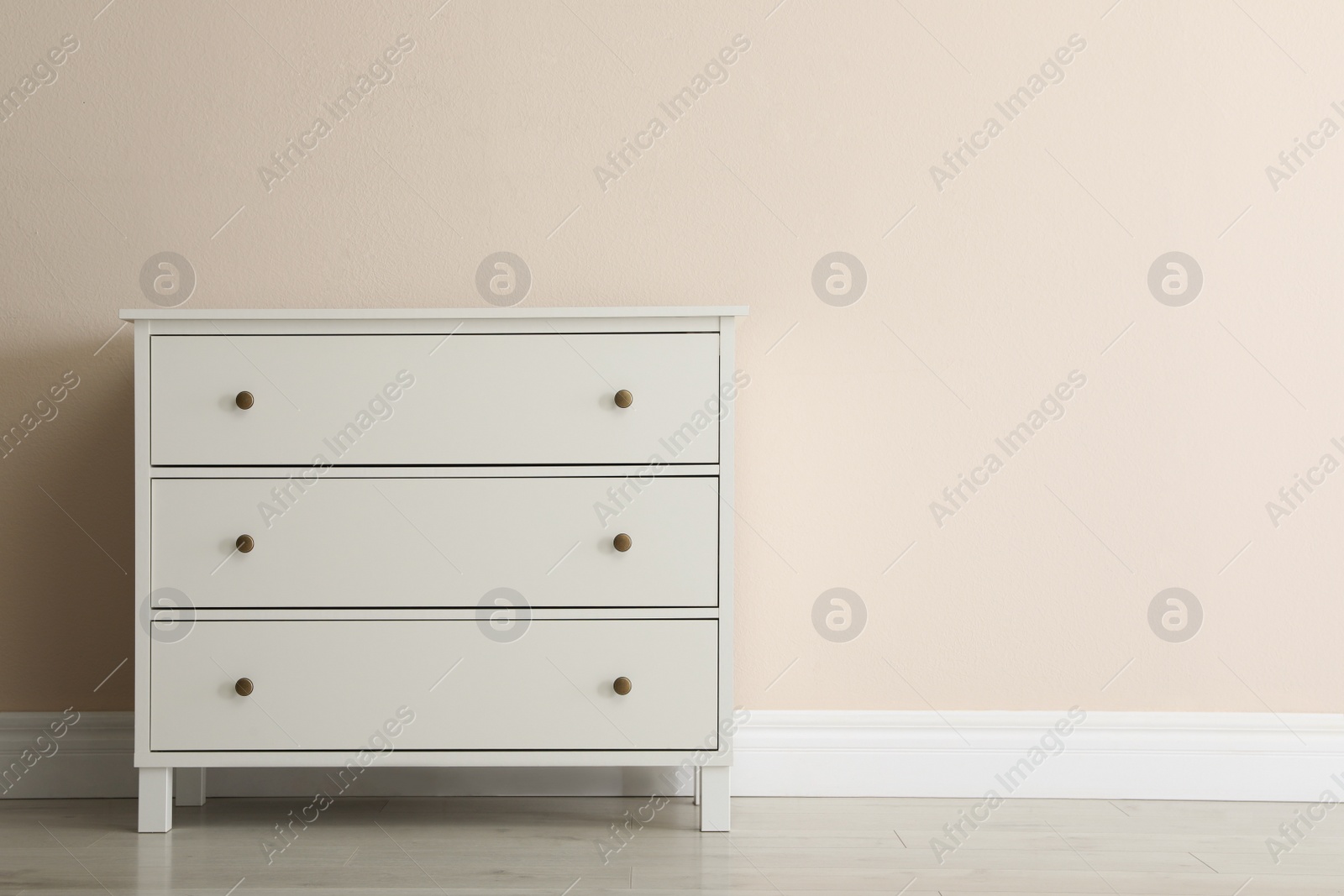 Photo of White chest of drawers near beige wall. Space for text
