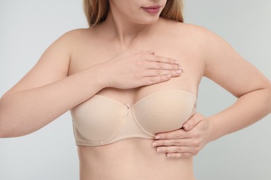 Mammology. Young woman doing breast self-examination on light grey background, closeup