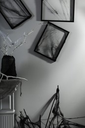 Photo of Black frames with cobweb on white wall and branches in vase decorated for Halloween indoors