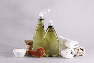 Bottles of cleaning product, brushes, rags and baking soda on light background