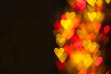 Blurred view of beautiful heart shaped lights on dark background