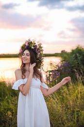 Photo of Young woman wearing wreath made of beautiful flowers outdoors at sunset