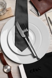 Photo of Business lunch concept. Plates, cutlery, tie, wallet and watch on wooden table, flat lay