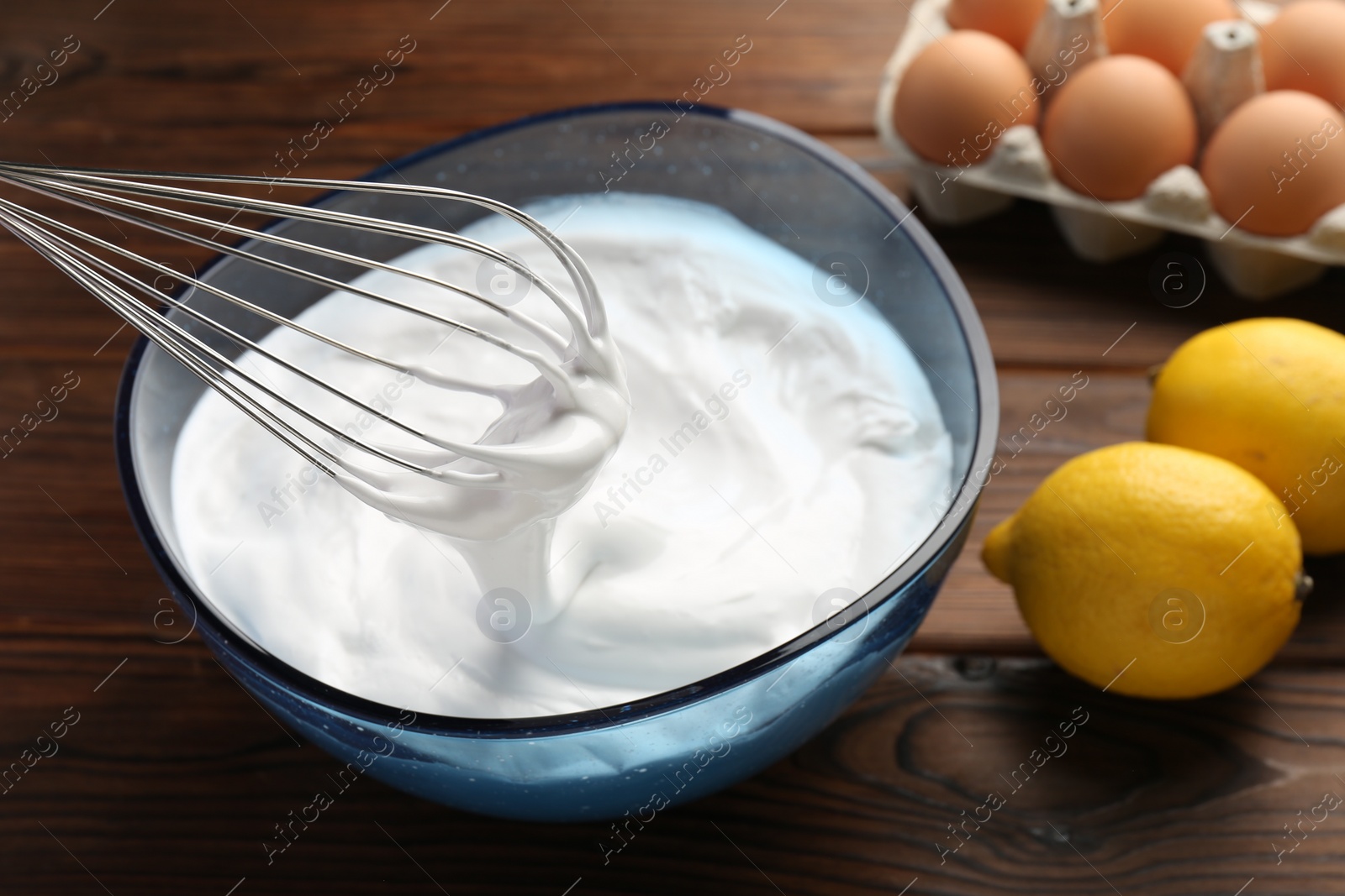 Photo of Bowl with whipped cream, whisk and ingredients on wooden table