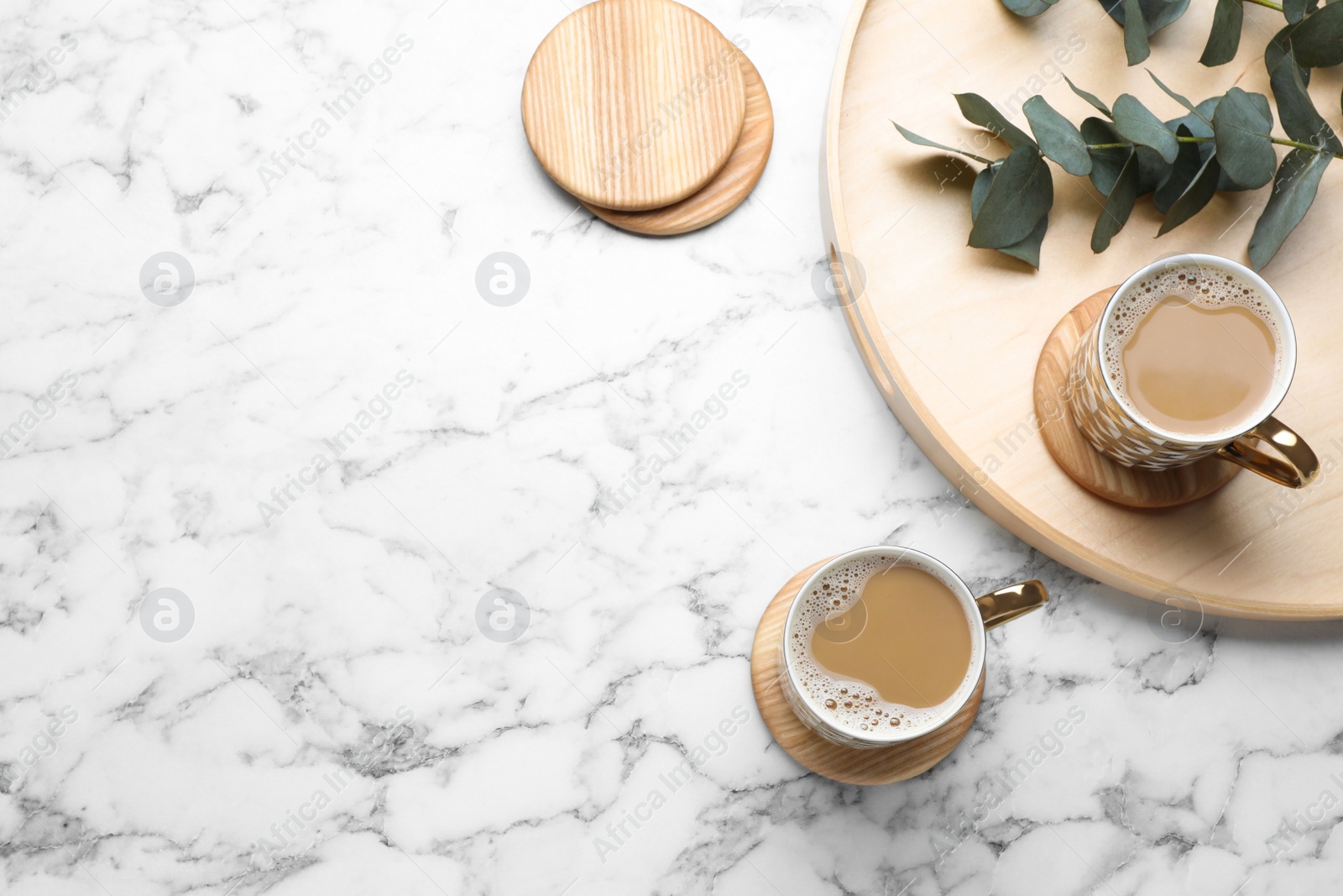 Photo of Mugs of coffee, stylish wooden cup coasters and eucalyptus branches on white marble table, flat lay. Space for text