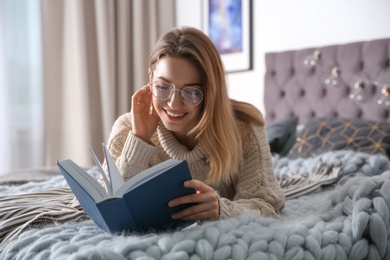 Photo of Young woman reading book on bed at home