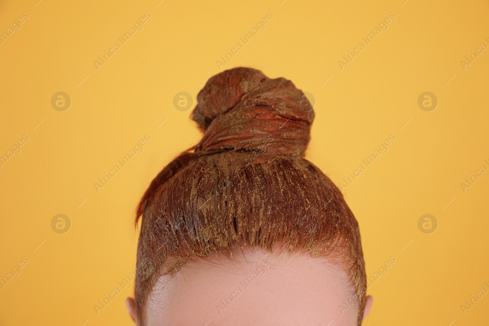 Photo of Young woman dyeing her hair with henna on yellow background, closeup