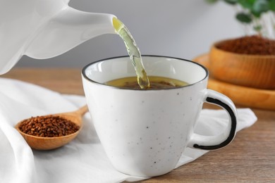 Photo of Pouring buckwheat tea into cup on wooden table, closeup