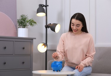 Young woman putting coin into piggy bank at home