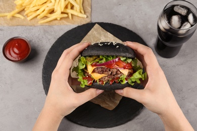 Photo of Woman holding black burger at served table, above view