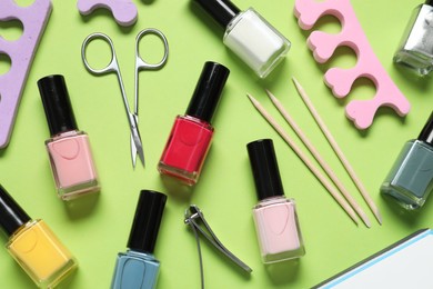Nail polishes and set of pedicure tools on green background, flat lay