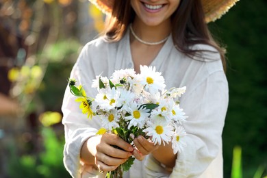 Photo of Woman holding bouquet of beautiful white chamomile flowers outdoors, closeup