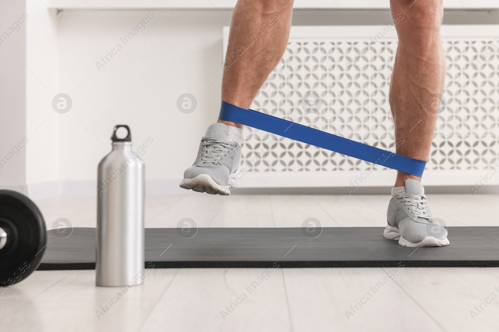 Photo of Athletic man doing exercise with elastic resistance band on mat indoors, closeup