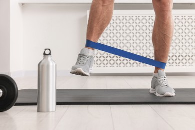 Athletic man doing exercise with elastic resistance band on mat indoors, closeup