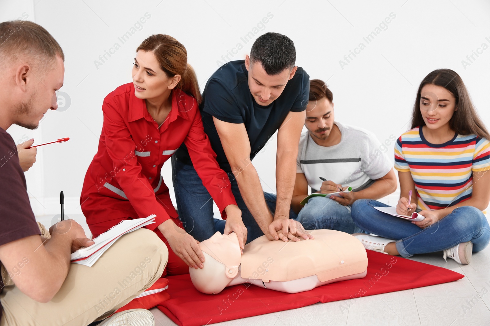 Photo of Group of people with instructor practicing CPR on mannequin at first aid class indoors