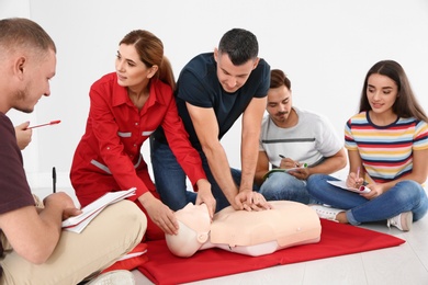 Group of people with instructor practicing CPR on mannequin at first aid class indoors