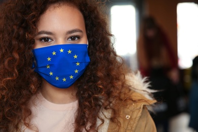 Image of African American woman wearing medical mask with European Union flag, outdoors. Coronavirus outbreak in Europe