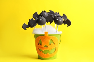 Photo of Delicious bat shaped cake pops on yellow background. Halloween treat