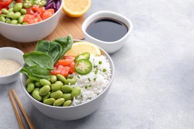 Photo of Poke bowl with salmon, edamame beans and rice on light grey table, space for text