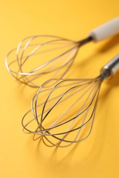 Two metal whisks on yellow background, closeup. Kitchen tool