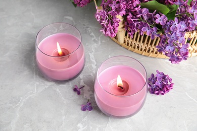 Photo of Burning wax candles in glass holders and lilac flowers on grey table