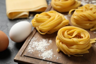 Photo of Raw tagliatelle pasta and products on black table, closeup