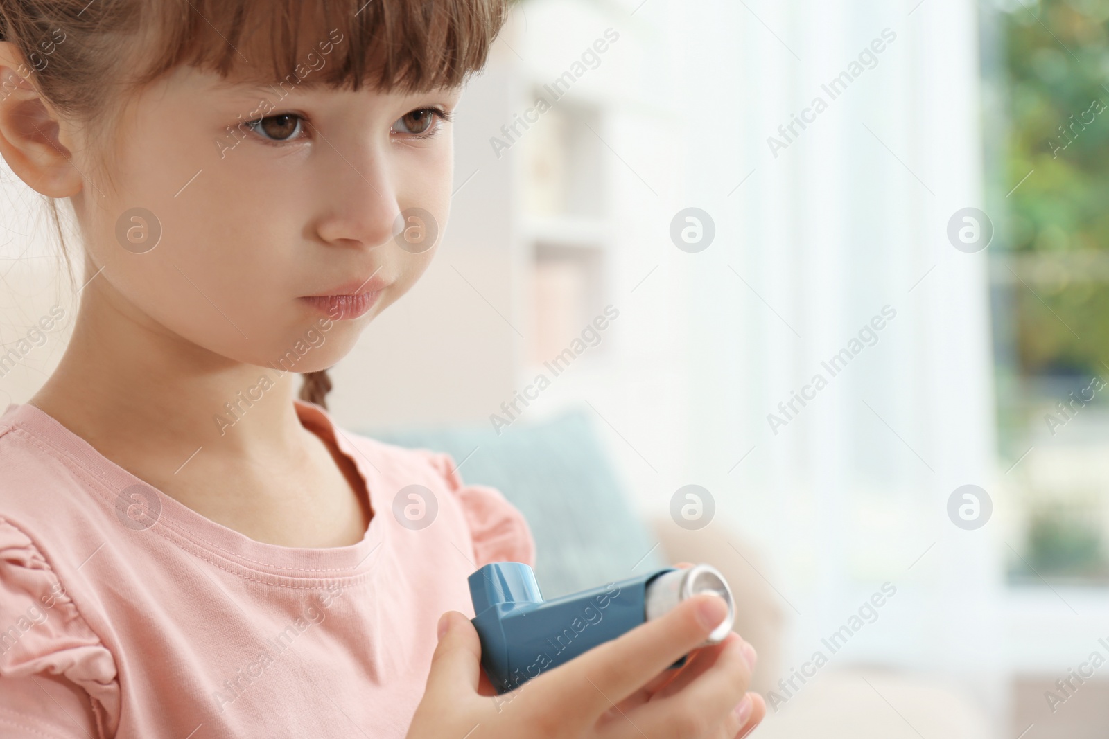 Photo of Little girl with asthma inhaler on blurred background