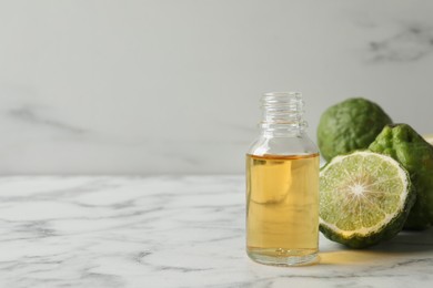 Bottle of essential oil and fresh bergamot fruits on white marble table. Space for text