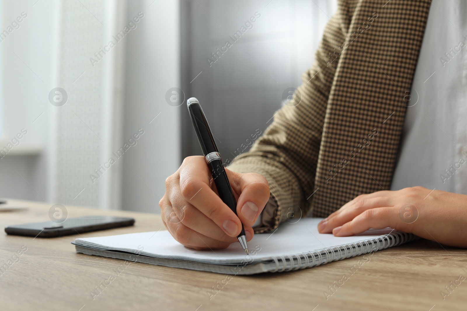 Photo of Woman writing in notebook at wooden table indoors, closeup