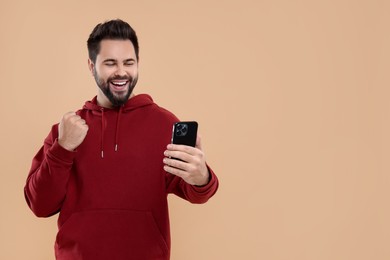 Happy young man using smartphone on beige background, space for text