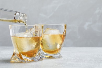 Pouring whiskey from bottle into glass at light table, closeup. Space for text