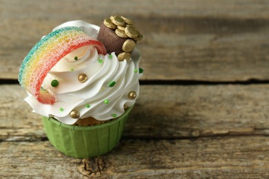 St. Patrick's day party. Tasty cupcake with sour rainbow belt and pot of gold toppers on wooden table, closeup. Space for text
